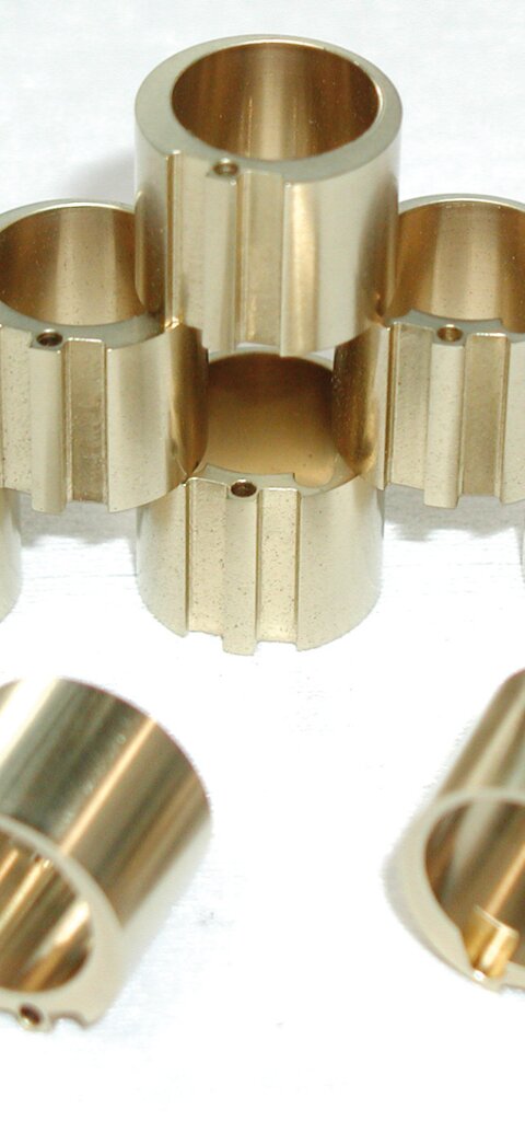 Stacked metallic cylindrical components with grooves and holes, arranged in a pyramid shape on a white background, featuring a DLC coating – PLASTIT® DLC, applied using PACVD technology. This 2 µm thick coating provides high hardness, excellent wear resistance, and reduced friction, ideal for mechanical engineering and automotive industry applications.